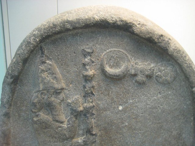 The rounded top of a stele in the British Museum showing a crowned figure beside divine symbols, identified on Commons as Nabonidus