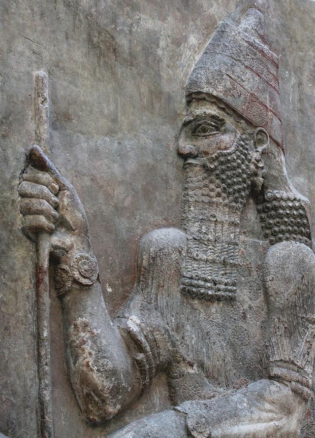 Sargon II in profile in a carved relief from Khorsabad, wearing a tall crown and holding a staff, in the Louvre