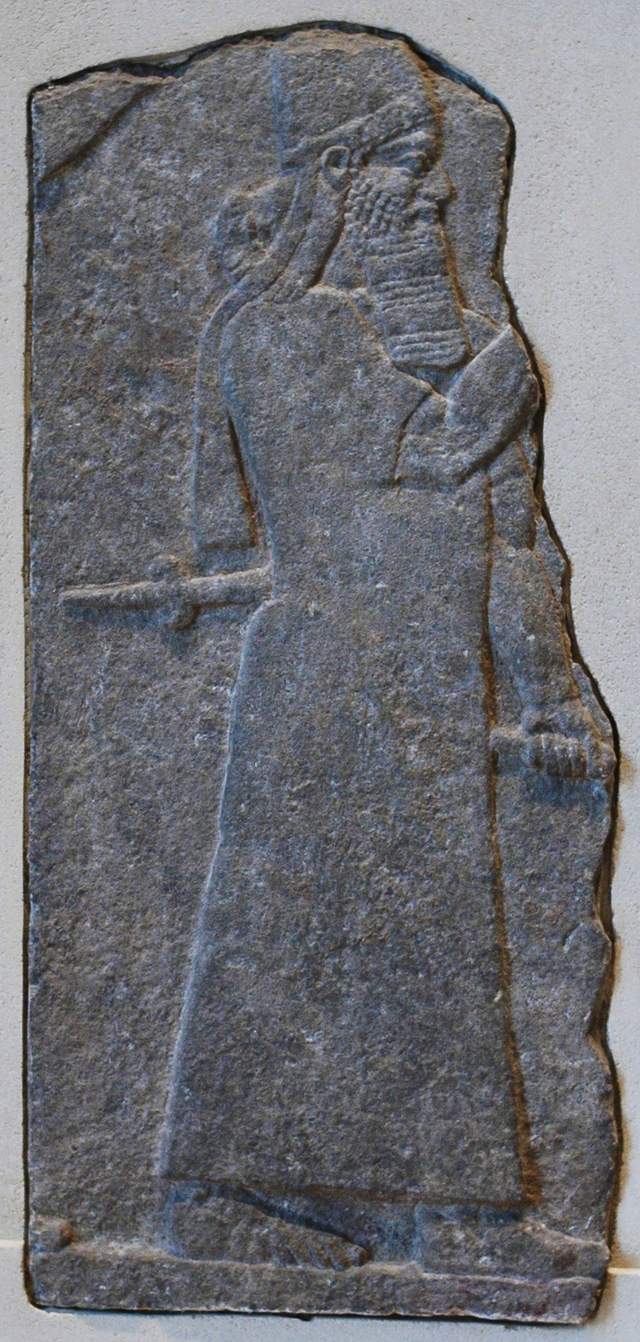 A carved relief from Nimrud in the Louvre of a bearded figure in profile in a long robe holding a sword, identified by the Louvre as Tiglath-pileser III