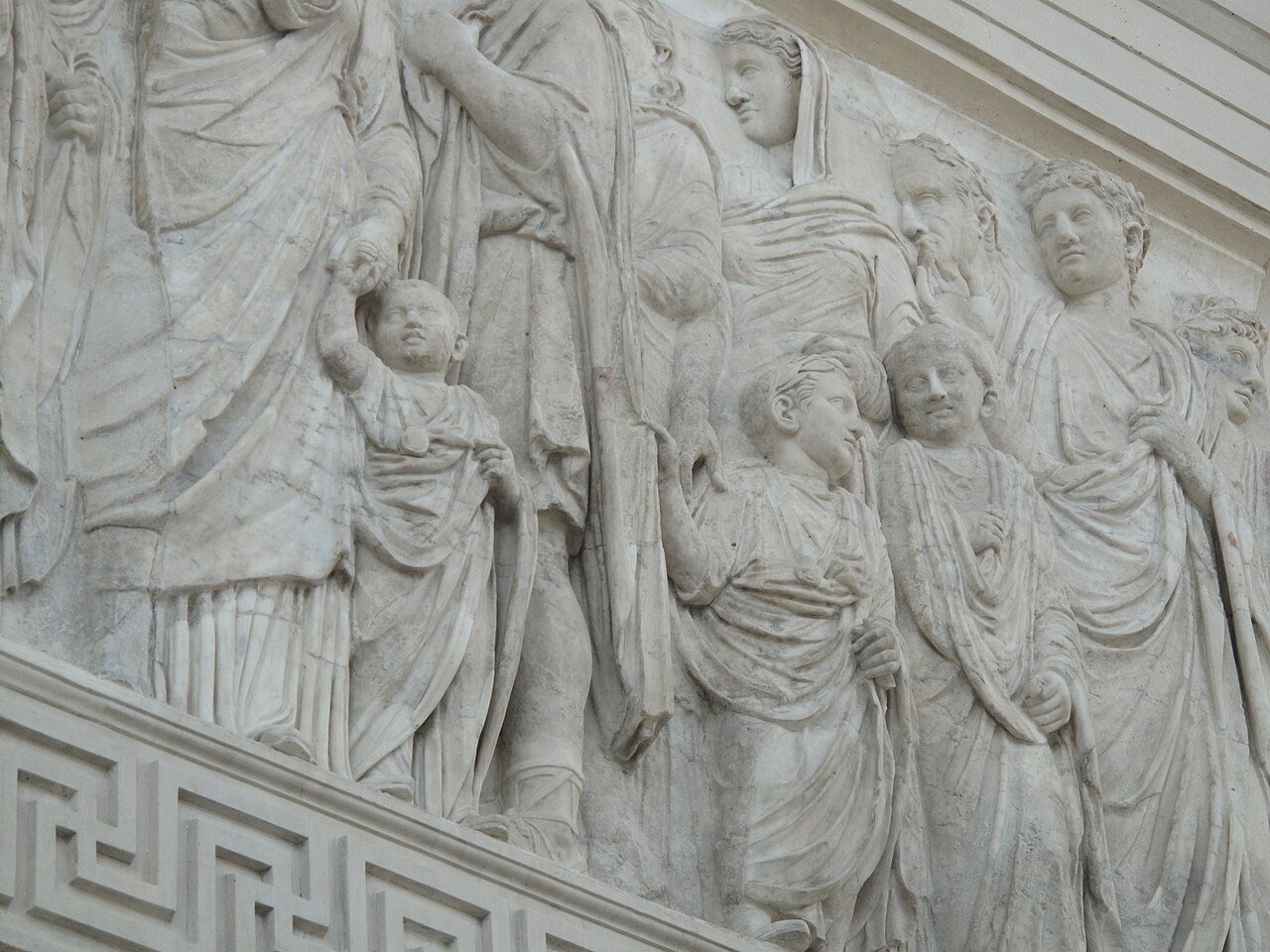 A marble relief of draped men, women and children in procession, with a Greek-key border along the foot