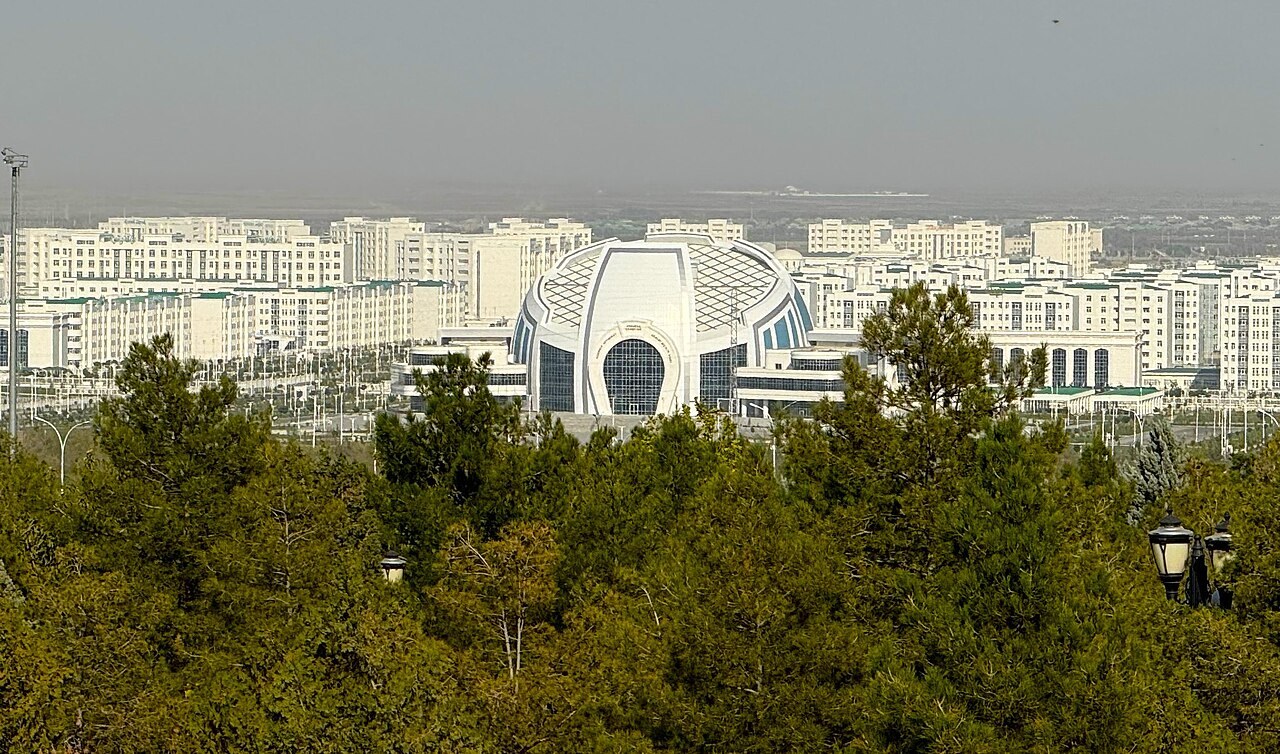 White apartment blocks and a white domed building with a blue-glass arch seen over trees