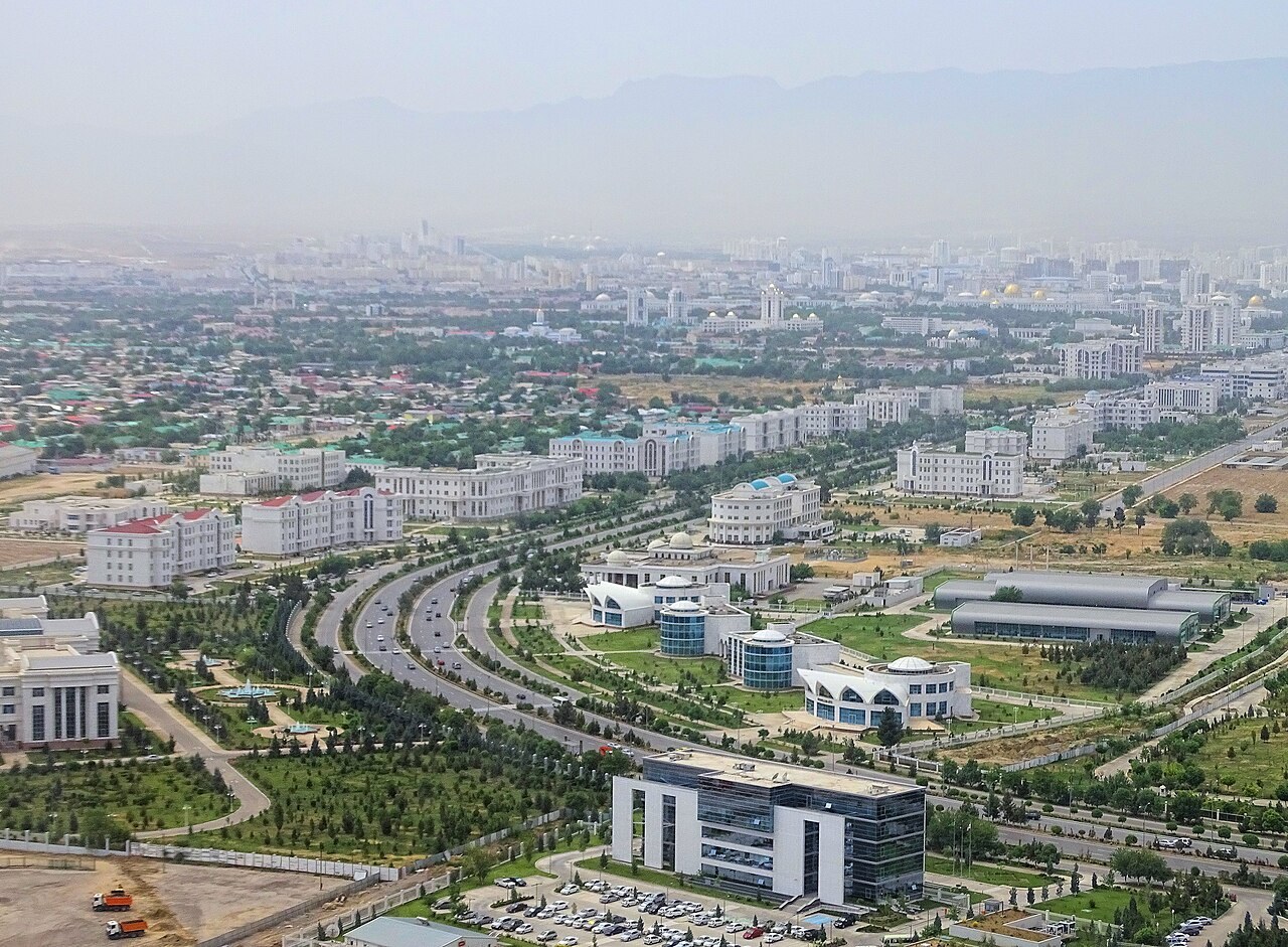 Aerial view of Ashgabat with a divided avenue and rows of white buildings below mountains