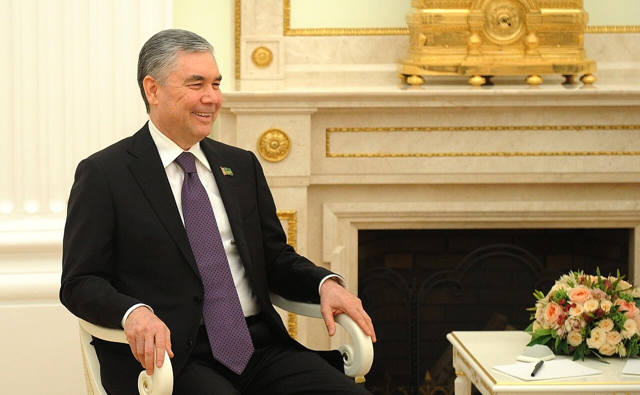 Gurbanguly Berdimuhamedov seated and smiling in a Kremlin room beside a marble fireplace and a bouquet