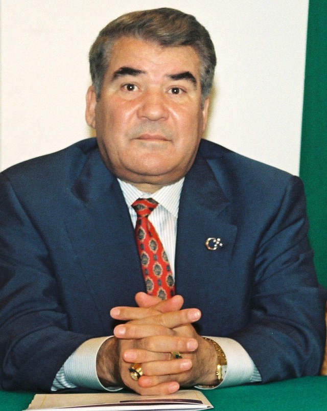 Saparmurat Niyazov seated at a table with clasped hands, in 1998