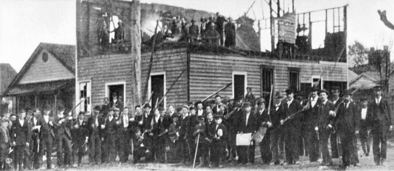 Armed white men standing in front of the burned-out Daily Record building, Wilmington, North Carolina, November 1898