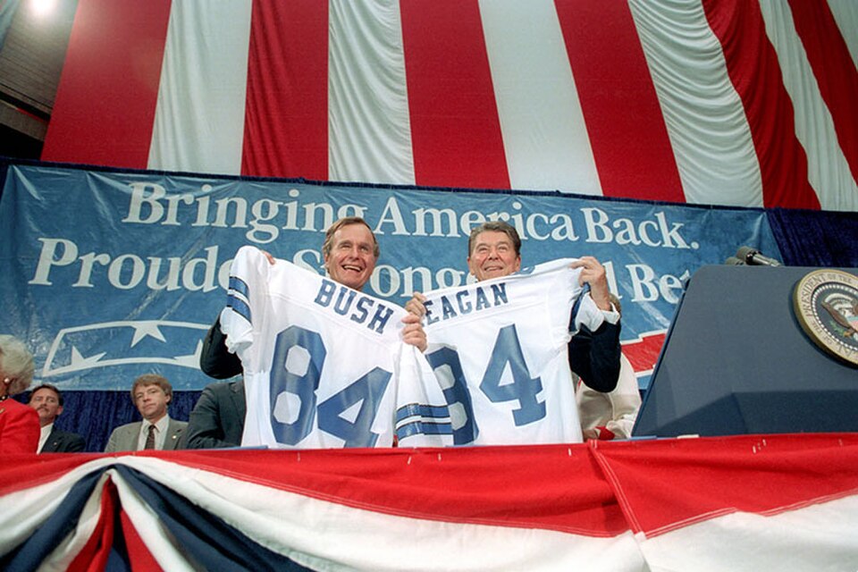Ronald Reagan and George H. W. Bush holding Dallas Cowboys jerseys in front of a banner reading "Bringing America Back. Prouder, Stronger, Better"